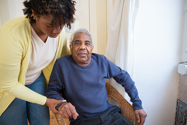 Woman Helping A Man Out Of His Chair